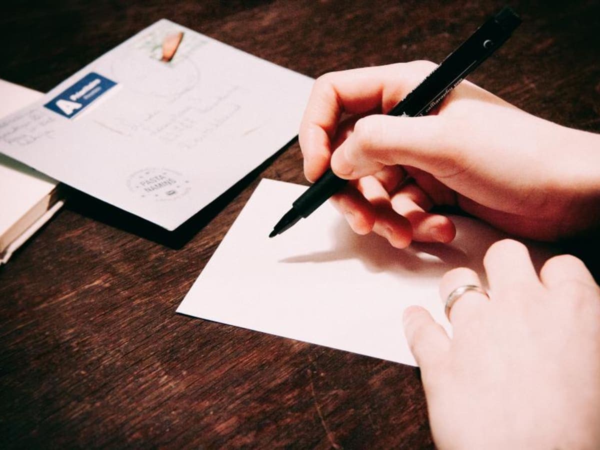 Hands writing on postcards at a wooden table.